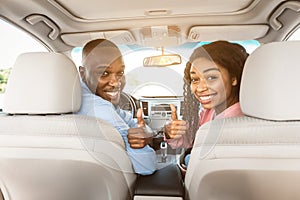 Happy black couple sitting in auto gesturing thumbs up