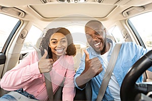 Happy black couple sitting in car gesturing thumbs up