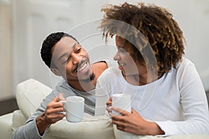 Happy black couple sitting on couch at home, drinking coffee