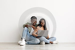 Happy black couple sitting on floor with laptop, having conversation