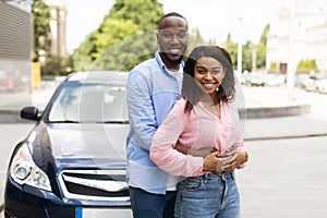 Happy black couple standing near car and hugging