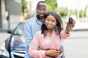 Happy black couple standing near car showing auto keys