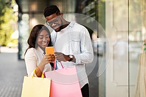 Happy black couple using phone holding shopping bags