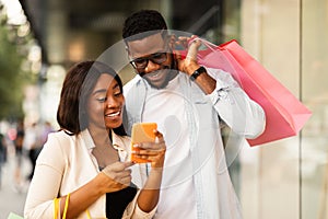 Happy black couple using phone with shopping bags