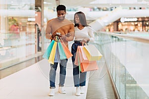 Happy black couple using phone walking with shopping bags