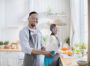 Happy black couple washing dishes together at kitchen, copy space. Family household duties concept