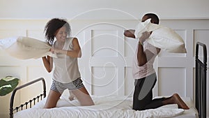 Happy black couple wear pajamas playing pillow fight on bed