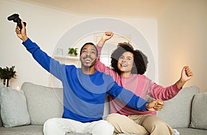 Happy Black Couple Winning Videogame Shaking Fists Sitting At Home