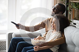 Happy black dad and daughter cuddle watching TV