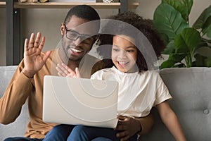 Happy black dad with kid daughter waving hands making videocall