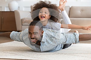 Happy black dad lying on floor with daughter on back.