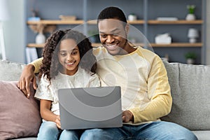 Happy black dad showing his daughter how to use computer