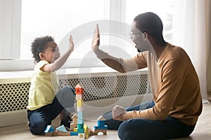 Happy black dad and toddler son giving high-five playing together photo