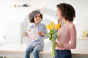 Happy black daughter greeting mom with tulips and card