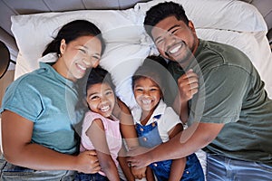 A happy black family in bed, mom and dad hold children with love. In their bedroom at home, little kids laugh as parents