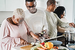 Happy black family cooking inside kitchen at home - Father, daughter, son and mother having fun preparing lunch - Main focus on