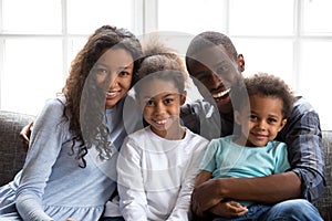 Happy black family of four looking at camera at home