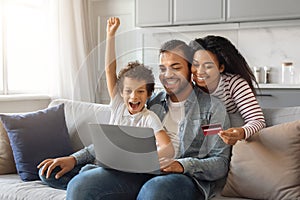 Happy Black Family With Laptop And Credit Card Making Shopping At Home
