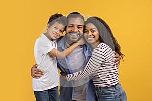 Happy black family with little son hugging and smiling brightly at camera