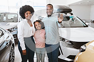 Happy black family posing with new car key, buying or renting automobile at auto dealership