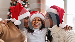 Happy black family in santa claus hats kissing, celebrating xmas