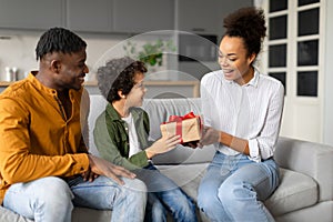 Happy black family sharing gift moment, with child receiving present from smiling parents
