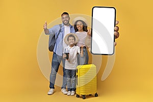 Happy Black Family With Suitcase And Tickets Showing Big Blank Smartphone