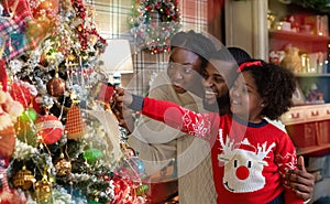 Happy black family of three decorating Christmas tree at home