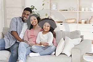 Happy black family of three hugging on couch and smiling