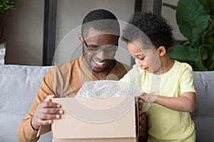 Happy black father and little kid son open cardboard box