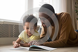 Happy black father and toddler son reading book at home