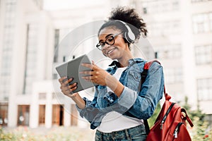 Happy Black Female Student Using Tablet Computer Wearing Headphones Outside