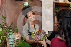 Happy black florist selling flowers to young woman