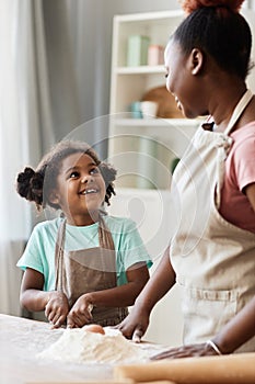 Happy black girl baking together with mother in cozy home kitchen