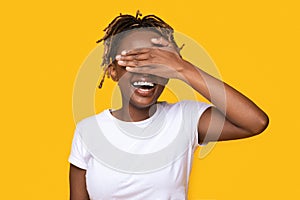 Happy black girl covering her eyes on yellow background