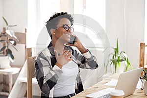 Happy black girl having pleasant smartphone talk at workplace