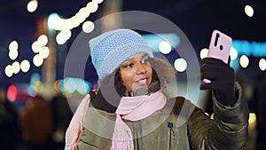 Happy black girl recording vlog on Christmas market at night