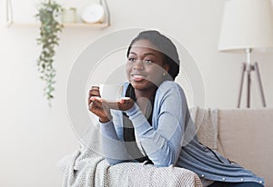 Happy black girl relaxing with cup of tea at home