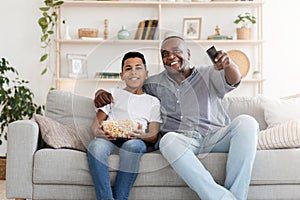 Happy black grandpa and his preteen grandson watching TV together at home