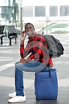 Happy black guy waiting at train station and using cellphone