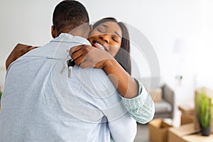 Happy black lady with keychain hugging her husband and smiling, celebrating moving to their house, free space