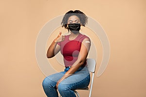 Happy black lady showing vaccinated arm with plaster after covid-19 vaccine injection, gesturing thumb up