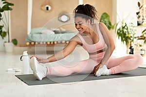 Happy black lady in sportswear exercising at home, stretching on fitness mat, touching her feet with hand, copy space