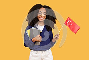 Happy black lady student with backpack and copybooks, holding a Chinese flag, on yellow background