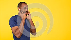 Happy Black Male Listening Music Wearing Earbuds Over Yellow Background