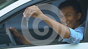 Happy black male teenager on driver place showing car keys, first automobile