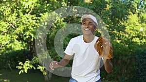 Happy black male teenager wearing white cap receiving and throwing baseball