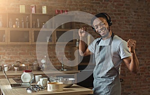 Happy black man listening to music and dancing in kitchen photo