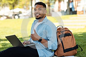 Happy black man gesturing like and using laptop, approving educational online program, sitting in park