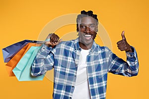 Happy black man holding colorful shopping bags and giving thumb up